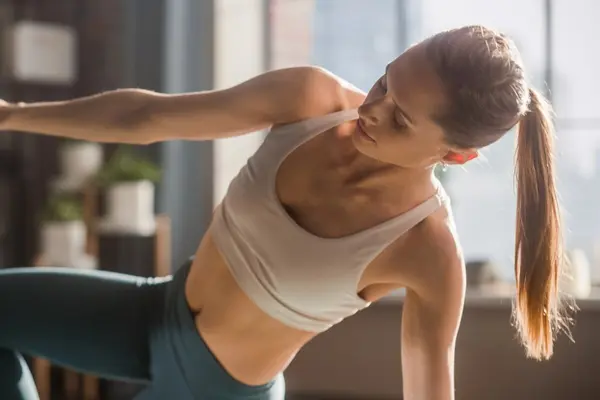 Close Up of Athletic Young Female Exercising, Stretching and Doing Yoga in the Morning in Her Bright Sunny Room at Home. Beautiful Woman in Sports Clothes Practising Different Asana Poses on the Mat.